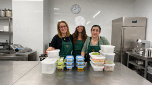 Tres mujeres en una cocina profesional con recipientes de comida preparada para organizar una alimentación equilibrada